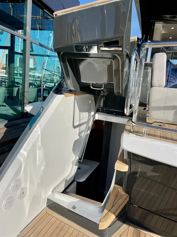 A modern boat's entrance hatch is opened, revealing steps leading below deck in a well-lit marina setting.